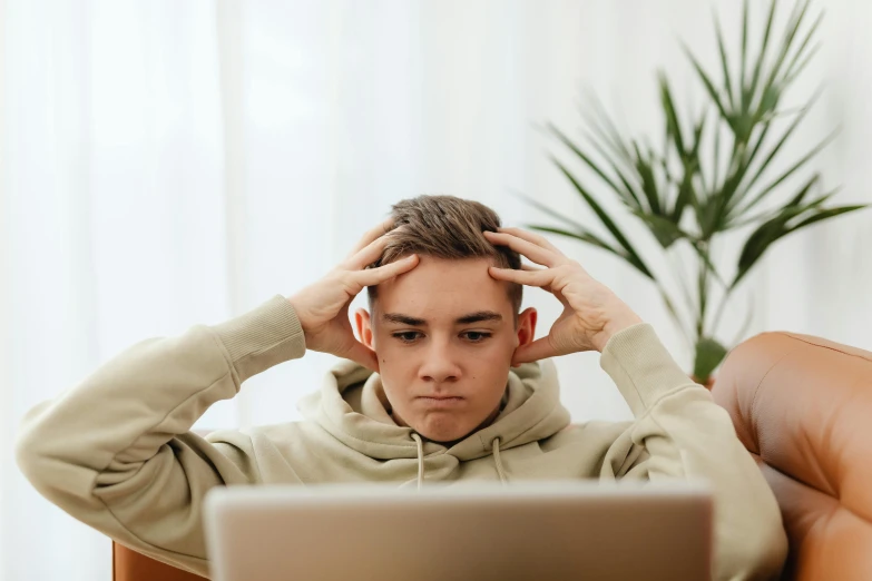 a young man sitting in front of a laptop computer, trending on pexels, paws on head, boy with neutral face, high forehead, casey cooke