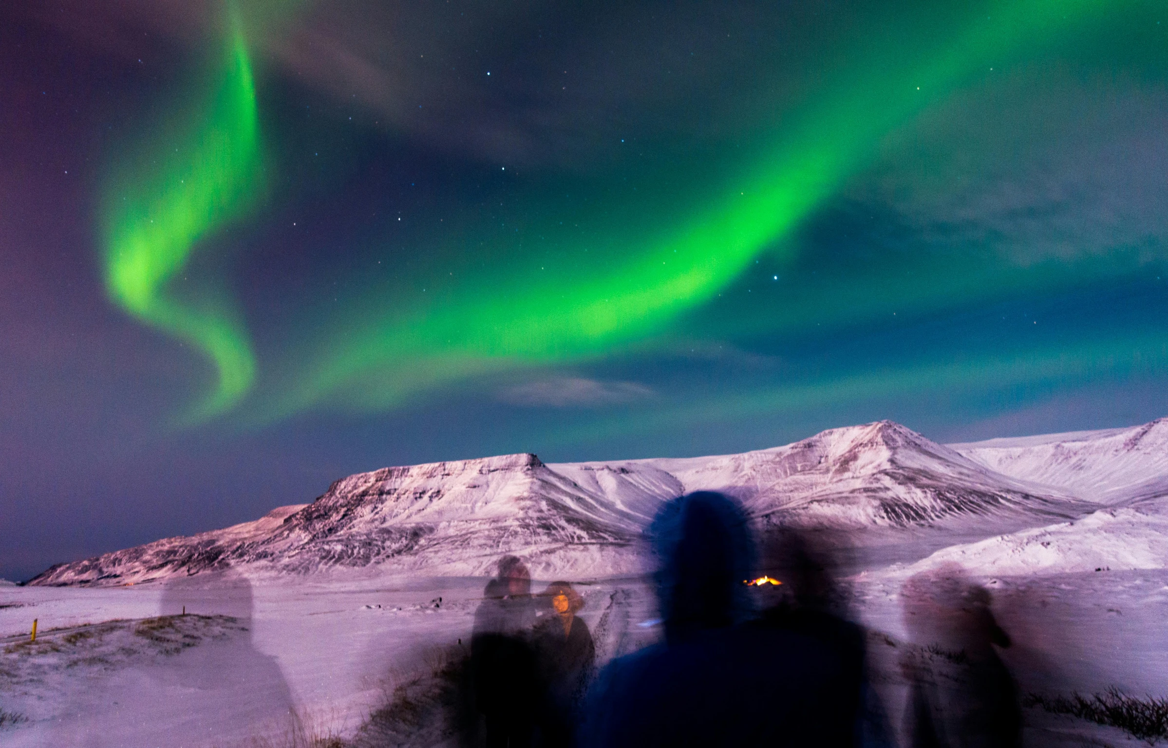 a group of people that are standing in the snow, by Julia Pishtar, pexels contest winner, hurufiyya, northen lights background, distant mountains lights photo, rim lights purple and green, conde nast traveler photo