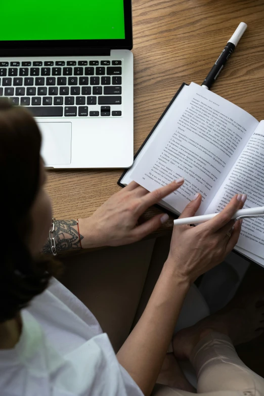 a woman sitting at a table with a laptop and a book, pexels contest winner, renaissance, top-down shot, teaching, low quality photo, closeup shot