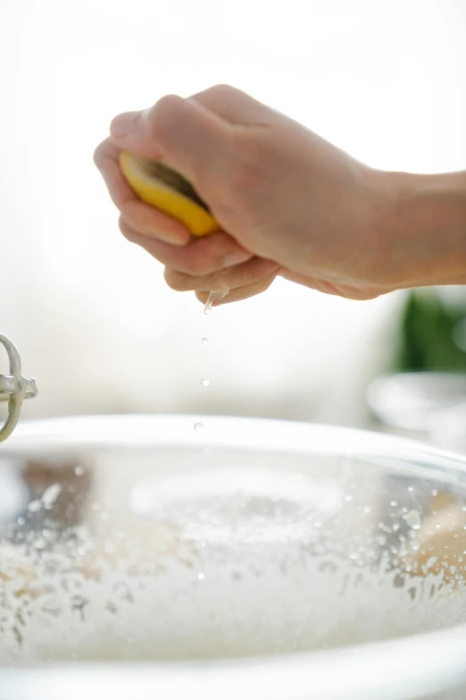 a person squeezing a lemon into a bowl of water, dust particles, stainless steal, epicurious, cleanest image