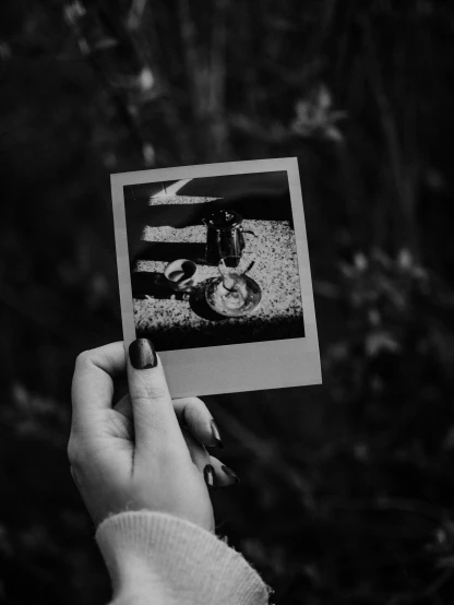 a person holding up a black and white photo, a polaroid photo, by Lucia Peka, pexels contest winner, polaroid photo of trailerpark, miscellaneous objects, dark and realistic, black & white