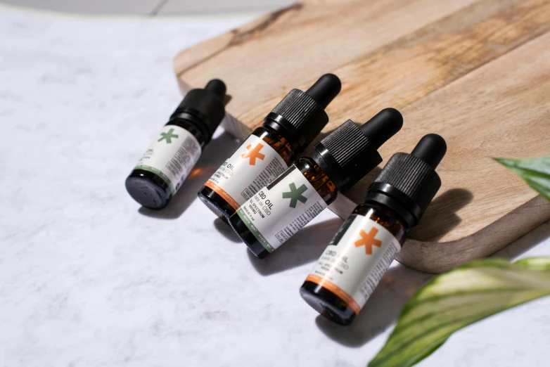 three bottles of cbd oil sitting on a cutting board, by Julia Pishtar, dark grey and orange colours, natural skin tones, orange and green power, exploration