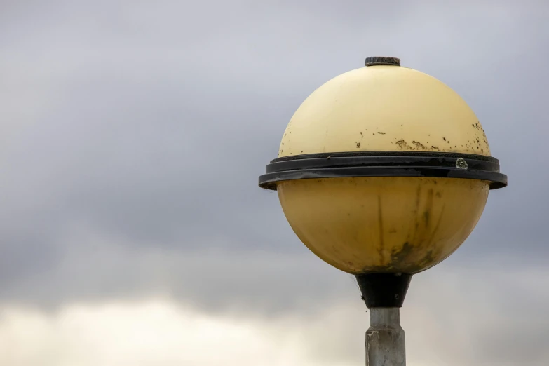 a close up of a street light with a cloudy sky in the background, inspired by Robert Bechtle, unsplash, photo of a dyson sphere, maryport, light yellow, on a pedestal