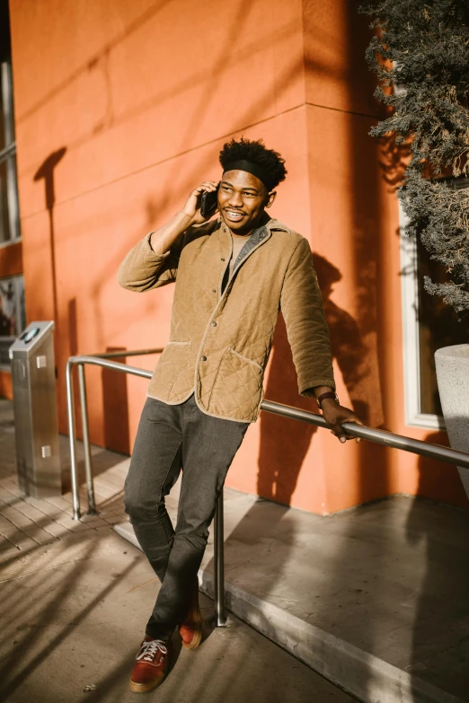 a man standing in front of a building talking on a cell phone, in style of tyler mitchell, brown clothes, corduroy, smiling man