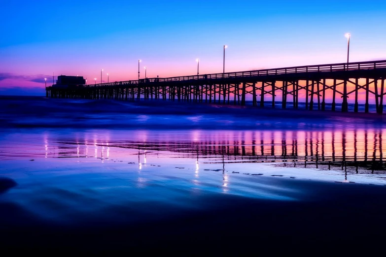 a pier sitting on top of a beach next to the ocean, pexels contest winner, red and blue reflections, purple and blue neons, bridge over the water, california;