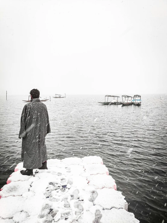 a man standing on top of a snow covered pier, by Lucia Peka, happening, wearing a grey robe, hangzhou, flooded fishing village, 2019 trending photo