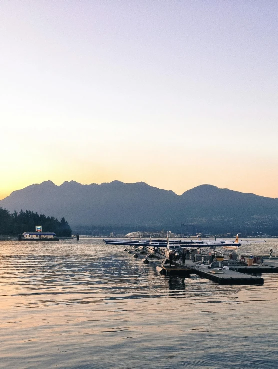 a group of boats floating on top of a lake, pexels contest winner, vancouver school, late summer evening, view from side, with mountains in background, docked at harbor