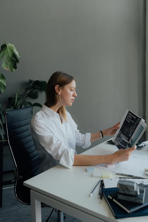 a woman sitting at a desk reading a book, a black and white photo, wearing a designer top, diagnostics, gif, profile image