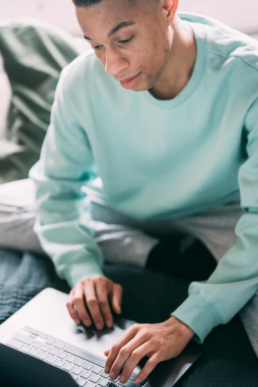 a woman sitting on a bed using a laptop, by James Morris, trending on pexels, teal uniform, wearing sweatshirt, pastels, a young man