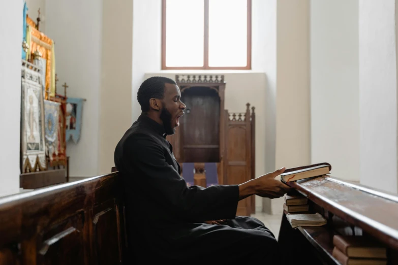 a man sitting in a church reading a book, an album cover, pexels, happening, mutahar laughing, pianist, black, priest