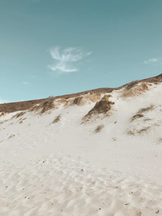 a man flying a kite on top of a sandy beach, an album cover, unsplash contest winner, land art, snow dunes, white and pale blue toned, australian beach, footprints in the sand