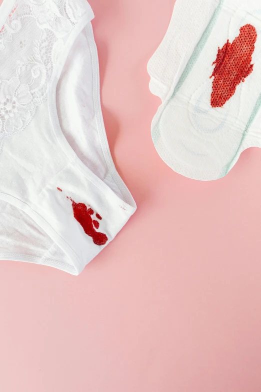 a pair of underwear sitting on top of a pink surface, a cross stitch, blood on body, made of lab tissue, white, product shot