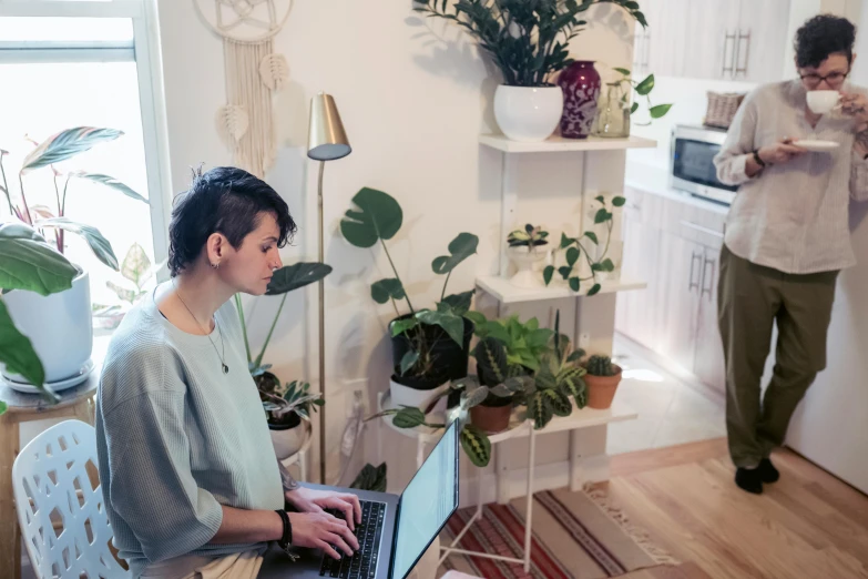 a woman sitting at a table using a laptop computer, by Liza Donnelly, unsplash, lush botany, standing in corner of room, casey cooke, profile image