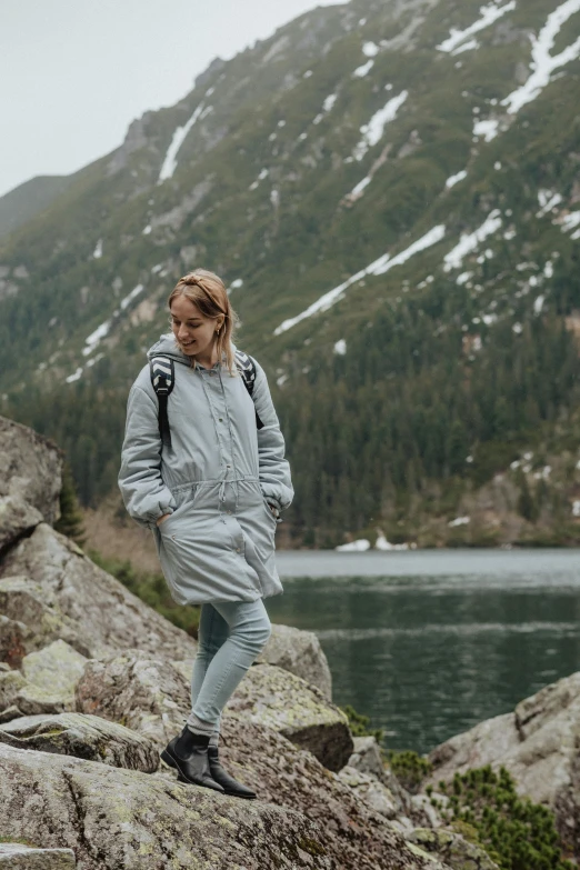 a woman standing on top of a rock next to a lake, inspired by Louisa Matthíasdóttir, pexels contest winner, model wears a puffer jacket, with two front pockets, light grey, whistler