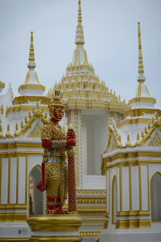 a statue in front of a white and gold building, a temple, in style of thawan duchanee, spines and towers, in 2 0 1 5