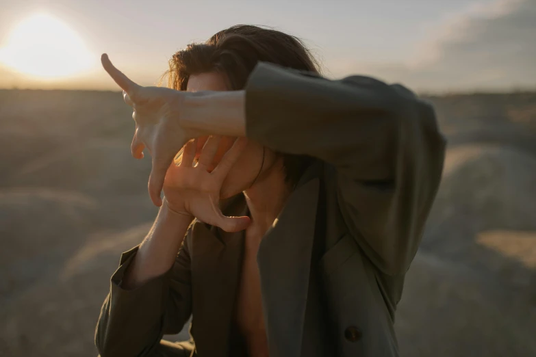 a woman covering her face with her hands, trending on pexels, surrealism, desert photography, androgynous male, late afternoon, pointing