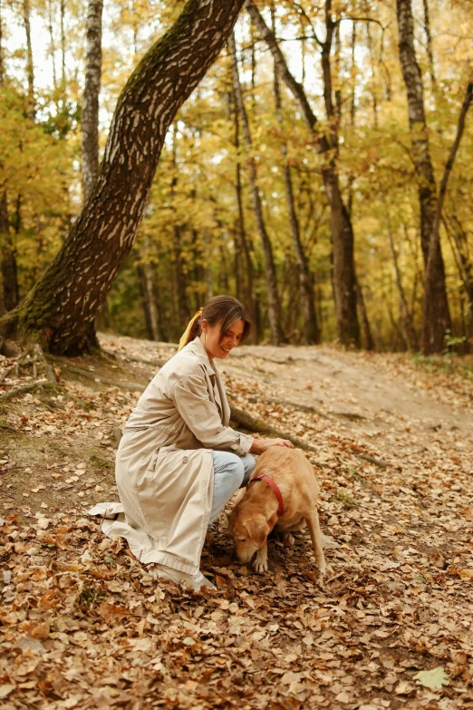 a woman sitting on the ground with a dog, in the woods, beige, amber, medium-shot