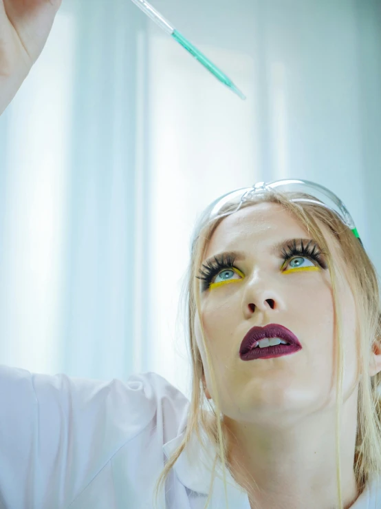 a woman in a lab coat holding a test tube, inspired by David LaChapelle, trending on pexels, magical realism, blonde hair blue eyes, bubble goth makeup, looking upwards, video still