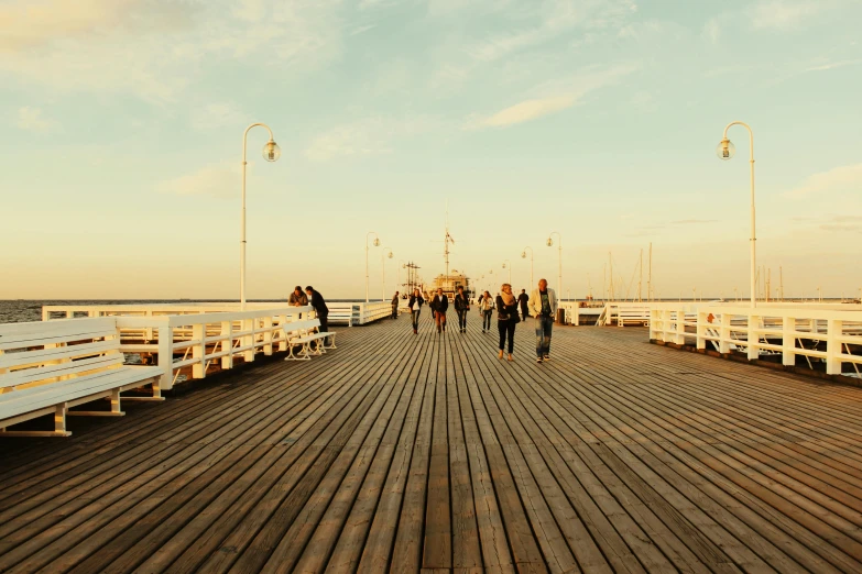 a group of people walking on a wooden pier, by Niko Henrichon, pexels contest winner, happening, soft warm light, brown, port city, sunfaded