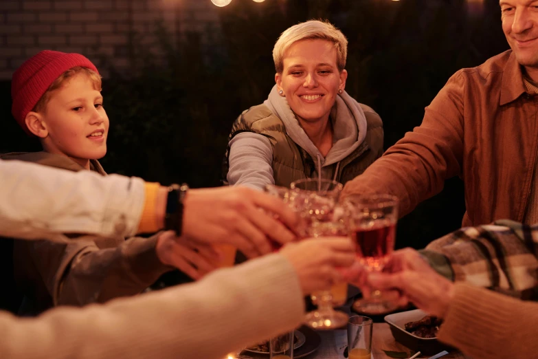 a group of people sitting around a table with wine glasses, outdoors at night, profile image, holiday season, guide