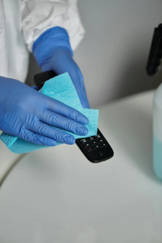 a person in blue gloves cleaning a cell phone, surgical supplies, television still, square, covid