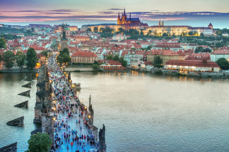 a group of people walking across a bridge over a river, by Matija Jama, pexels contest winner, renaissance, prague in the background, aerial, summer evening, multicoloured