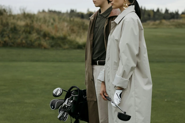 a couple of people standing next to each other on a field, unsplash, renaissance, golf digest, trenchcoat, clubs, uniform off - white sky