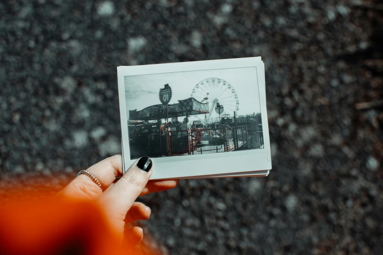 a person holding a picture of a ferris wheel, a polaroid photo, pexels contest winner, very old photo, theme park, picture frames, diary on her hand