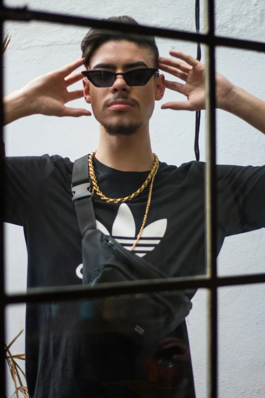 a man that is standing in front of a window, an album cover, inspired by Carlos Berlanga, unsplash, wearing gold chain, addidas, wearing an eyepatch, wearing a black t-shirt