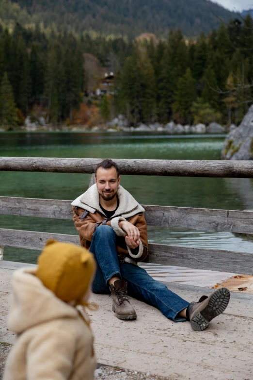 a man sitting on the ground next to a little girl, a picture, inspired by Ludovit Fulla, pexels contest winner, lake in the background, handsome man, lumberjack, on a bridge