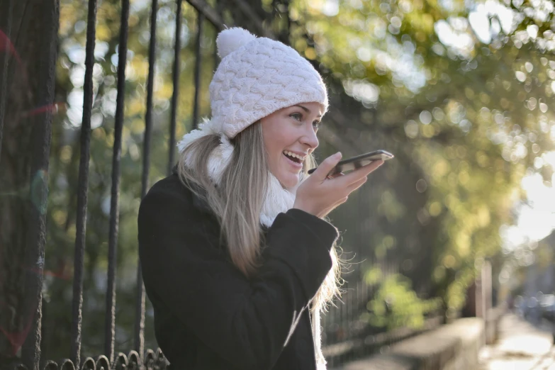 a woman smiles while looking at her cell phone, inspired by Amelia Robertson Hill, pexels contest winner, knitted hat, white, side profile view, holding a bell