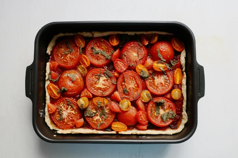 a close up of a pan of food on a table, by Emma Andijewska, one tomato slice, pastry, on grey background, assemble