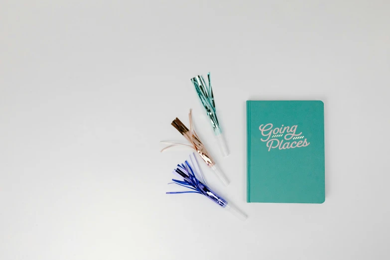 a blue notebook sitting on top of a white table, an album cover, inspired by Gina Pellón, trending on unsplash, glow sticks, tassels, oh the places you'll go, set against a white background