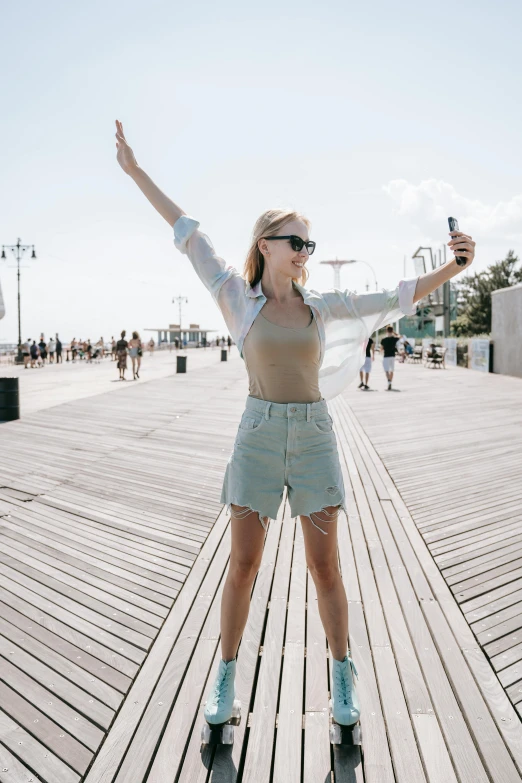 a woman riding a skateboard on top of a wooden boardwalk, a picture, trending on unsplash, happening, taking a selfie, bra and shorts streetwear, in new york, erin moriarty