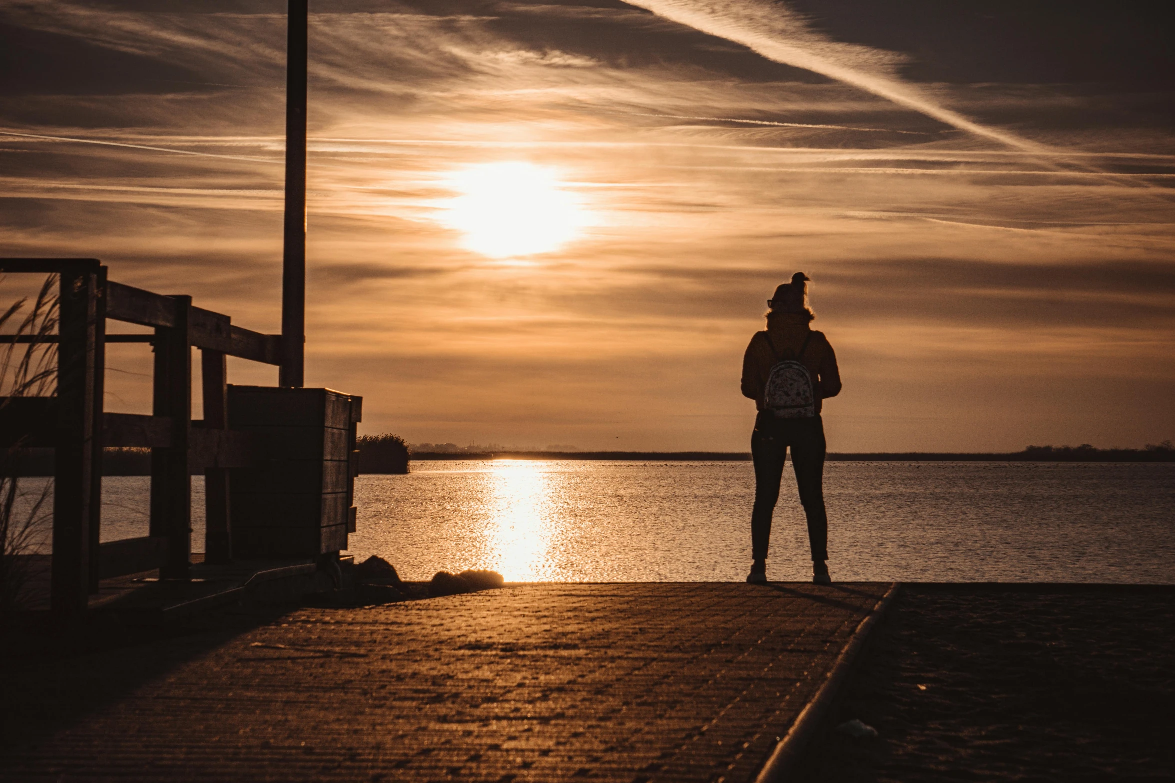 a person standing on a dock next to a body of water, by Niko Henrichon, pexels contest winner, golden hour 8k, street photo, fan favorite, silhouette :7