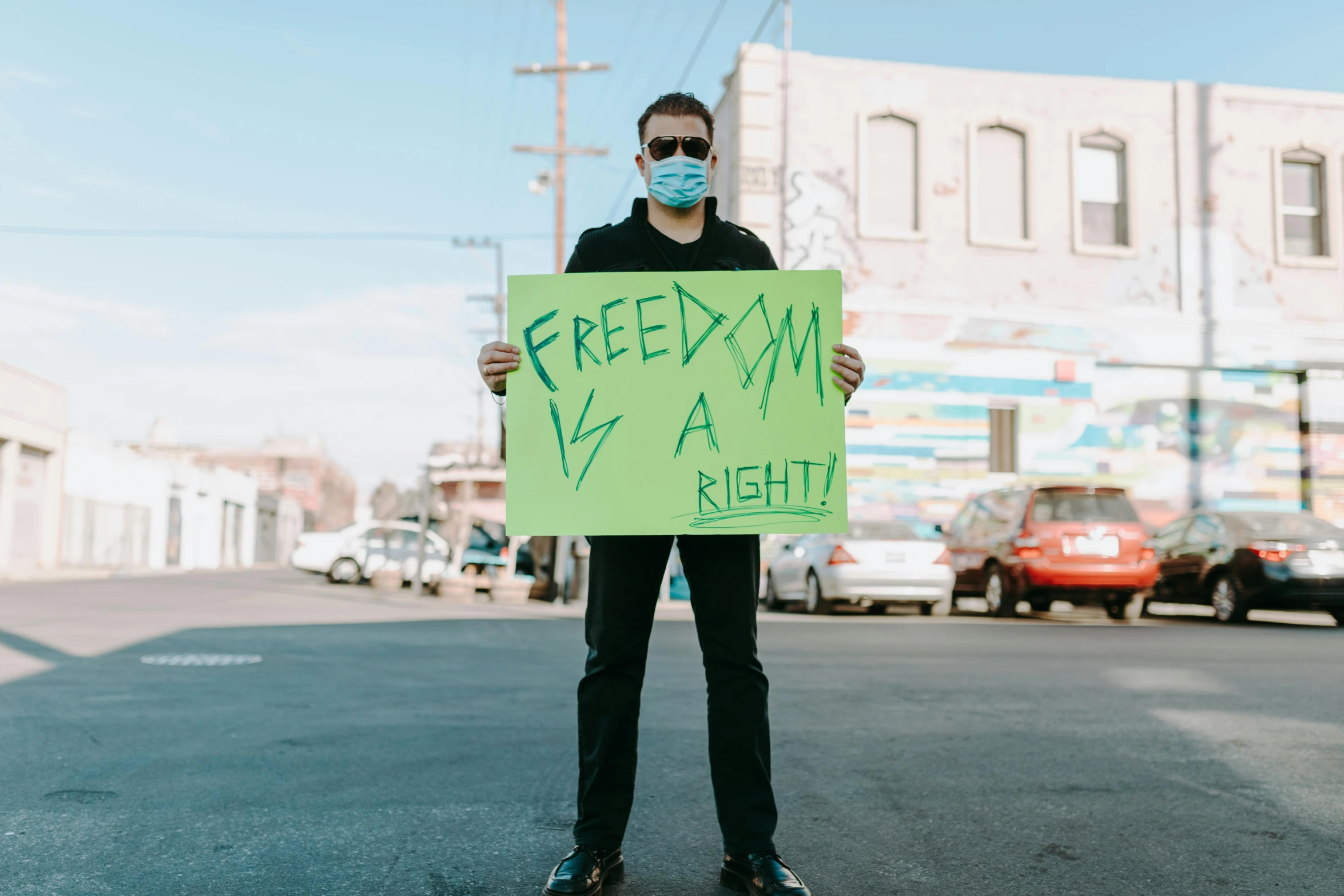 a man in a face mask holding a sign, an album cover, by Julia Pishtar, trending on pexels, freedom fighter, california;, gay rights, a green