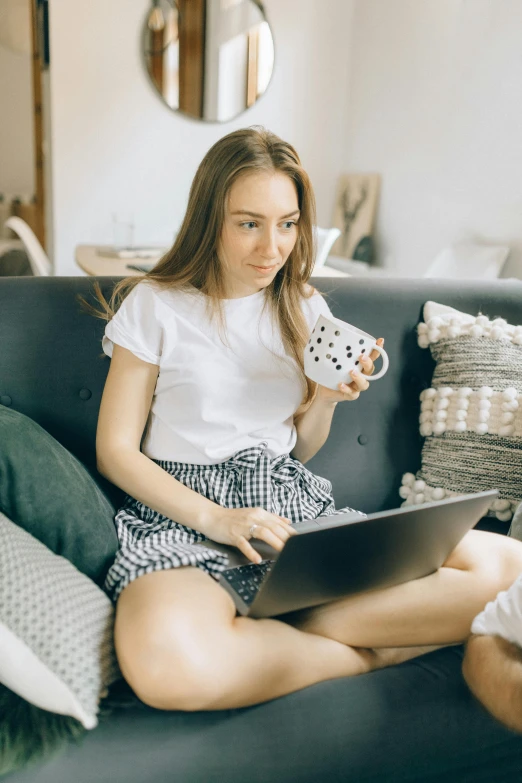 a woman sitting on a couch using a laptop, pexels contest winner, dressed in a top and shorts, with a white mug, anna podedworna, avatar image