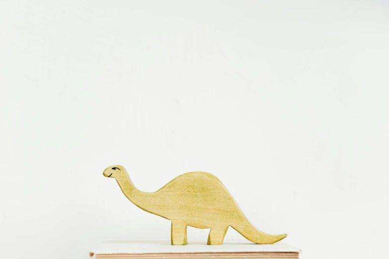 a wooden dinosaur sitting on top of a stack of books, a marble sculpture, trending on unsplash, painted pale yellow and green, product display photograph, petite pear slim figure, on the white background