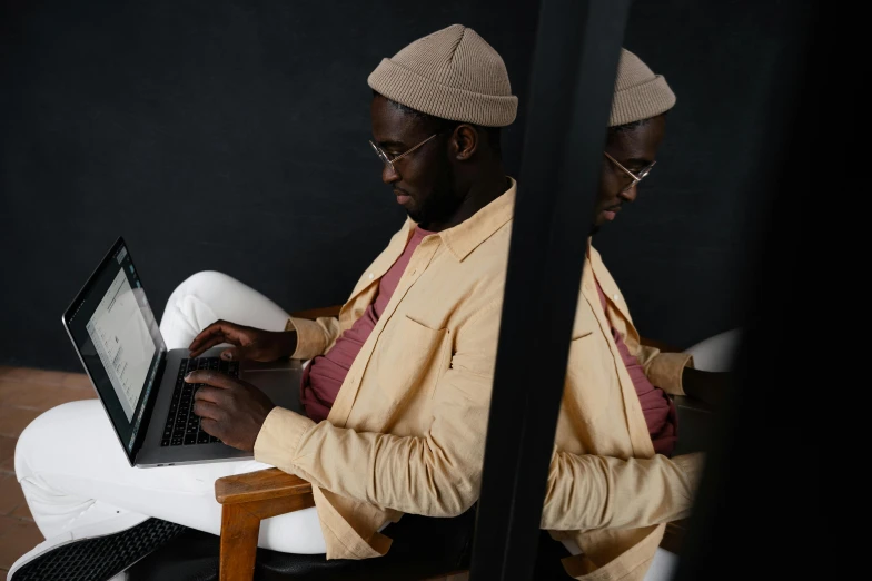 a man sitting in a chair using a laptop computer, a photo, by Carey Morris, trending on pexels, afrofuturism, brown clothes, looking into a mirror, yellow clothes, wearing elegant casual clothes