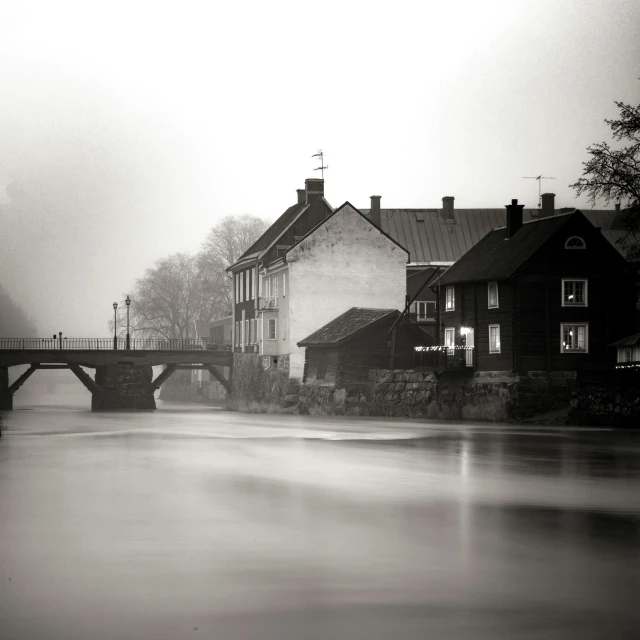 a black and white photo of a bridge over a river, by Jesper Myrfors, pexels contest winner, tonalism, quaint village, brown mist, medium format, swedish house