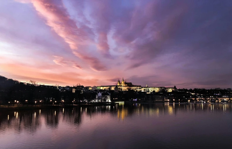 a large body of water with a castle in the background, by Antoni Brodowski, pexels contest winner, pink clouds in the sky, prague in the background, in the evening, graphic print