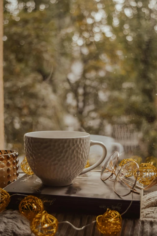 a coffee cup sitting on top of a wooden table, pexels contest winner, gold decorations, rainy window, seasonal, vanilla