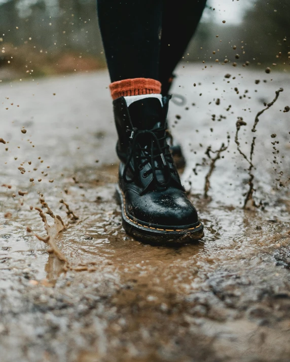 a person standing in a puddle of water, doc marten boots, kicking up dirt, black veins, top selection on unsplash