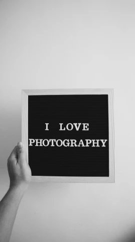 a person holding up a sign that says i love photography, a black and white photo, art photography, photography hight quality, low quality photo, beautiful realistic photo, - i