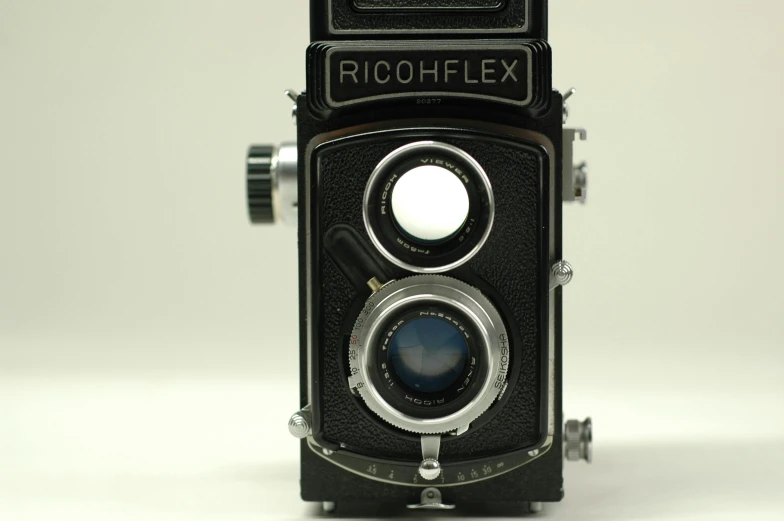 a close up of a camera on a white surface, a portrait, flickr, photorealism, rolleiflex, richly textured, a middle-shot from front, black