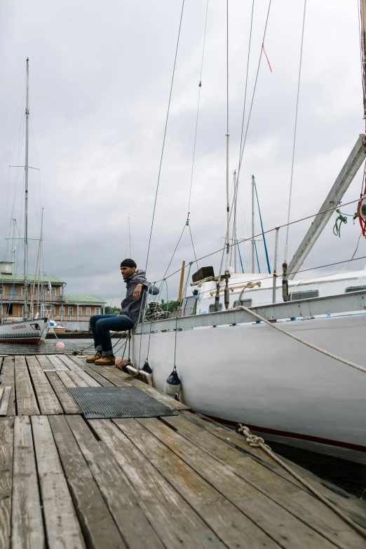 a man sitting on top of a boat on a dock, a portrait, unsplash, process art, sails and masts and rigging, overcast day, ballard, panorama shot