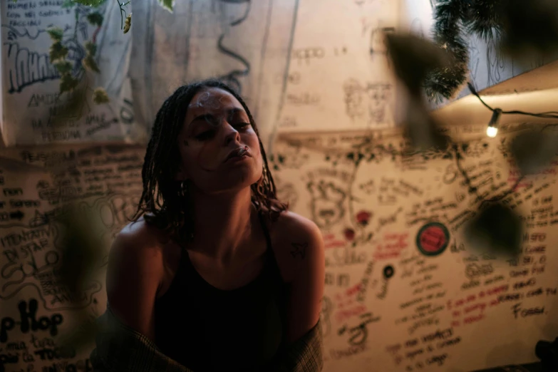 a woman standing in front of a wall with writing on it, a portrait, inspired by Elsa Bleda, pexels contest winner, ayahuasca, movie still of a tired, honey dripping from ceiling, evening time