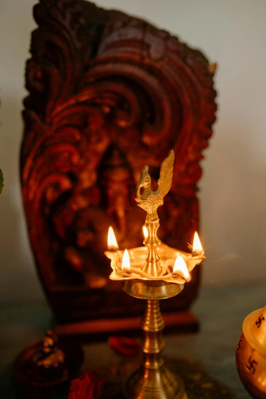 a couple of candles sitting on top of a table, a statue, with kerala motifs, emerging from a lamp