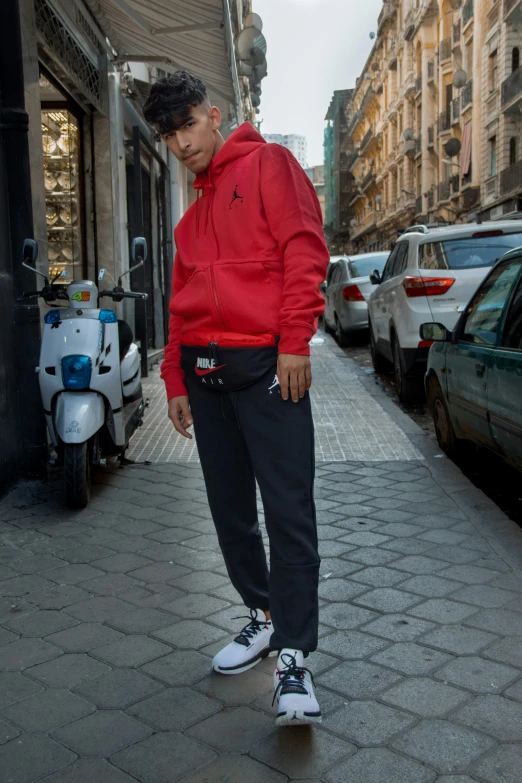 a man riding a skateboard down a sidewalk, inspired by Luis Molinari, wearing a scarlet hoodie, model posing, with two front pockets, wearing adidas clothing