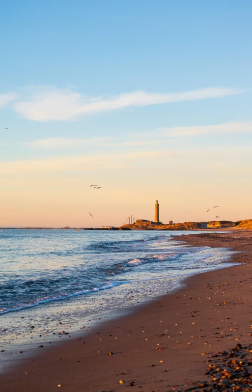 a sandy beach with a lighthouse in the distance, morning golden hour, historical setting